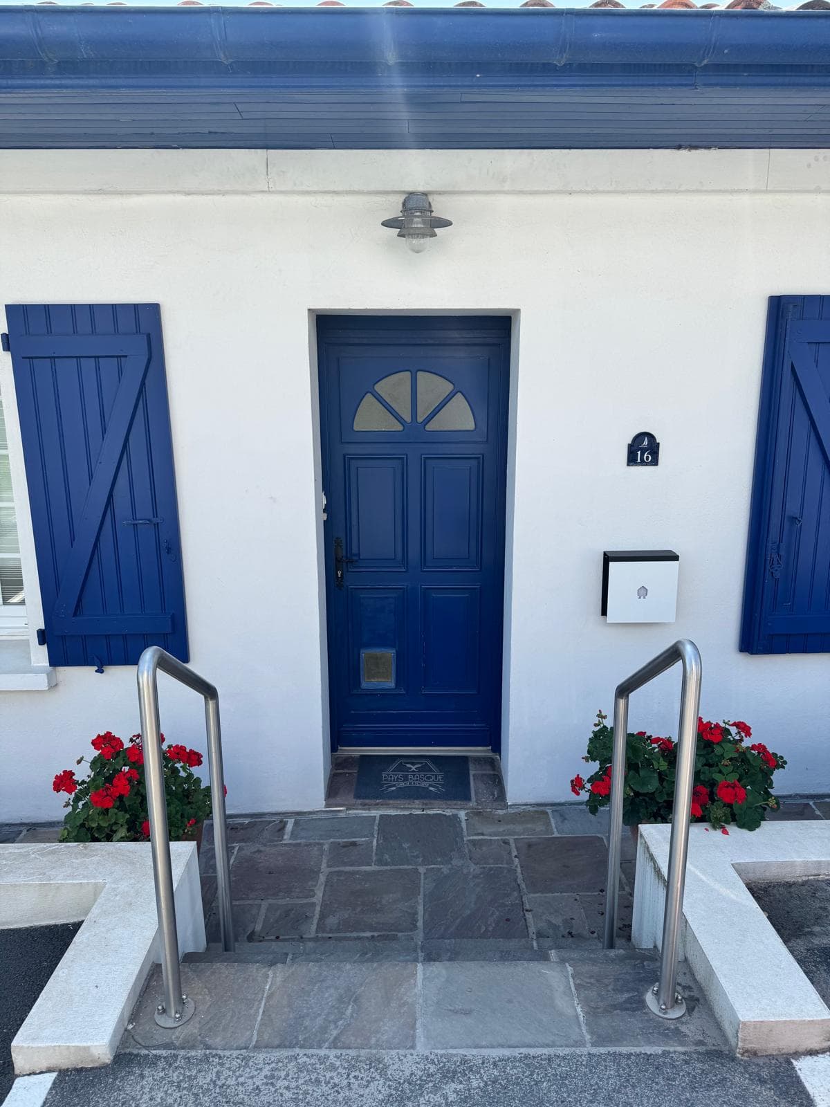 Façade complète centrée sur la porte bleue d'entrée et les volets, harmonie maison basque
