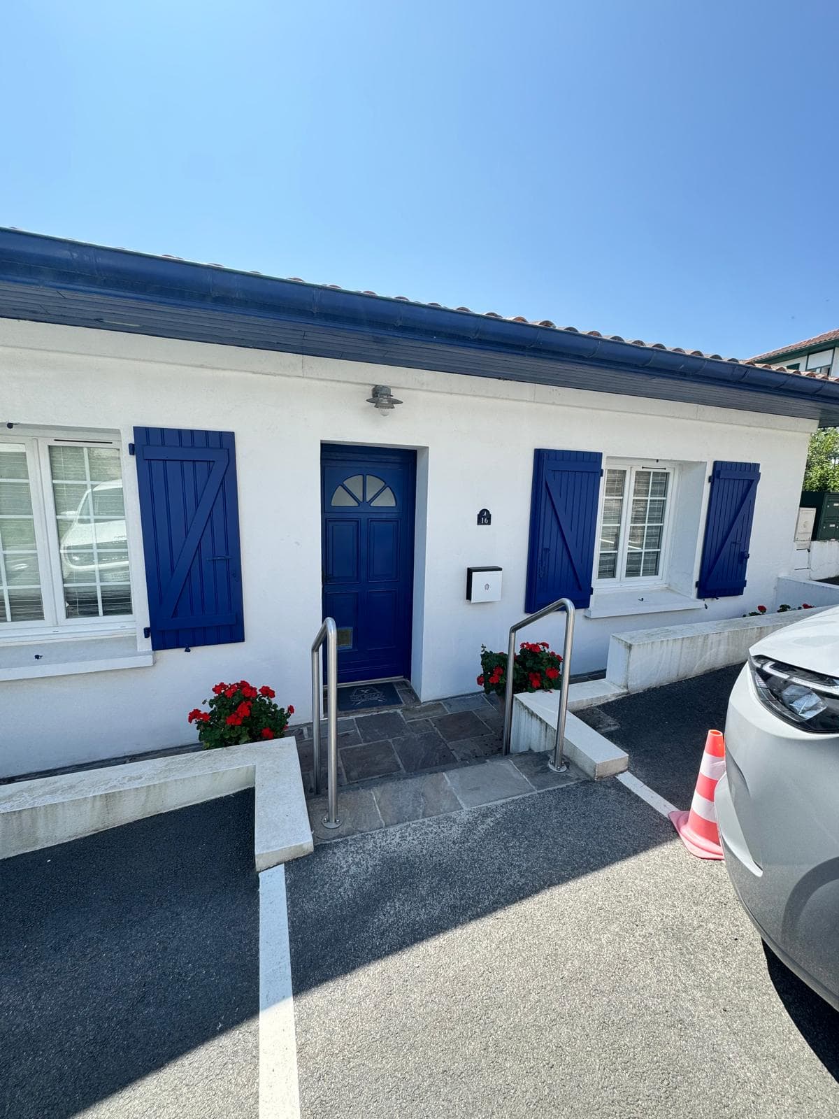 Vue depuis le parking, façade basque blanche à volets bleus avec accès à la borne