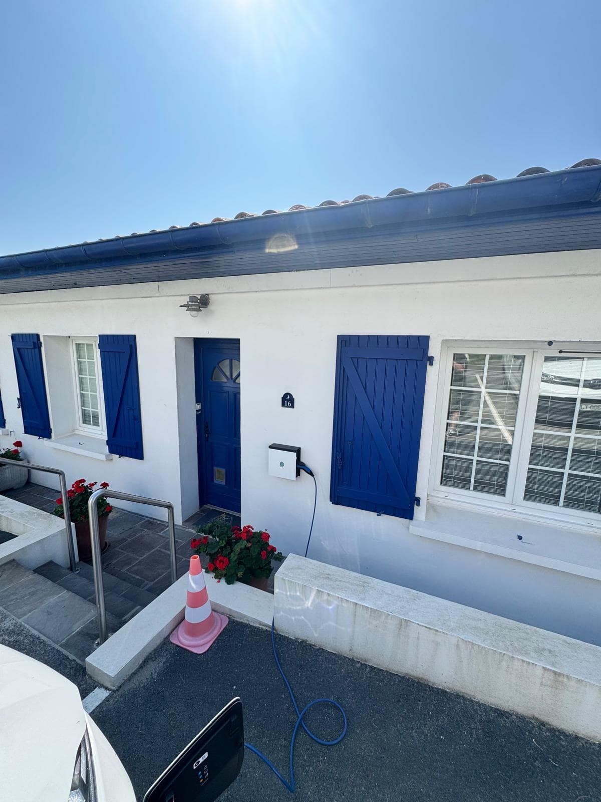 Vue d'ensemble de la façade ensoleillée avec borne Smappee EV Wall blanche installée à côté de la porte bleue